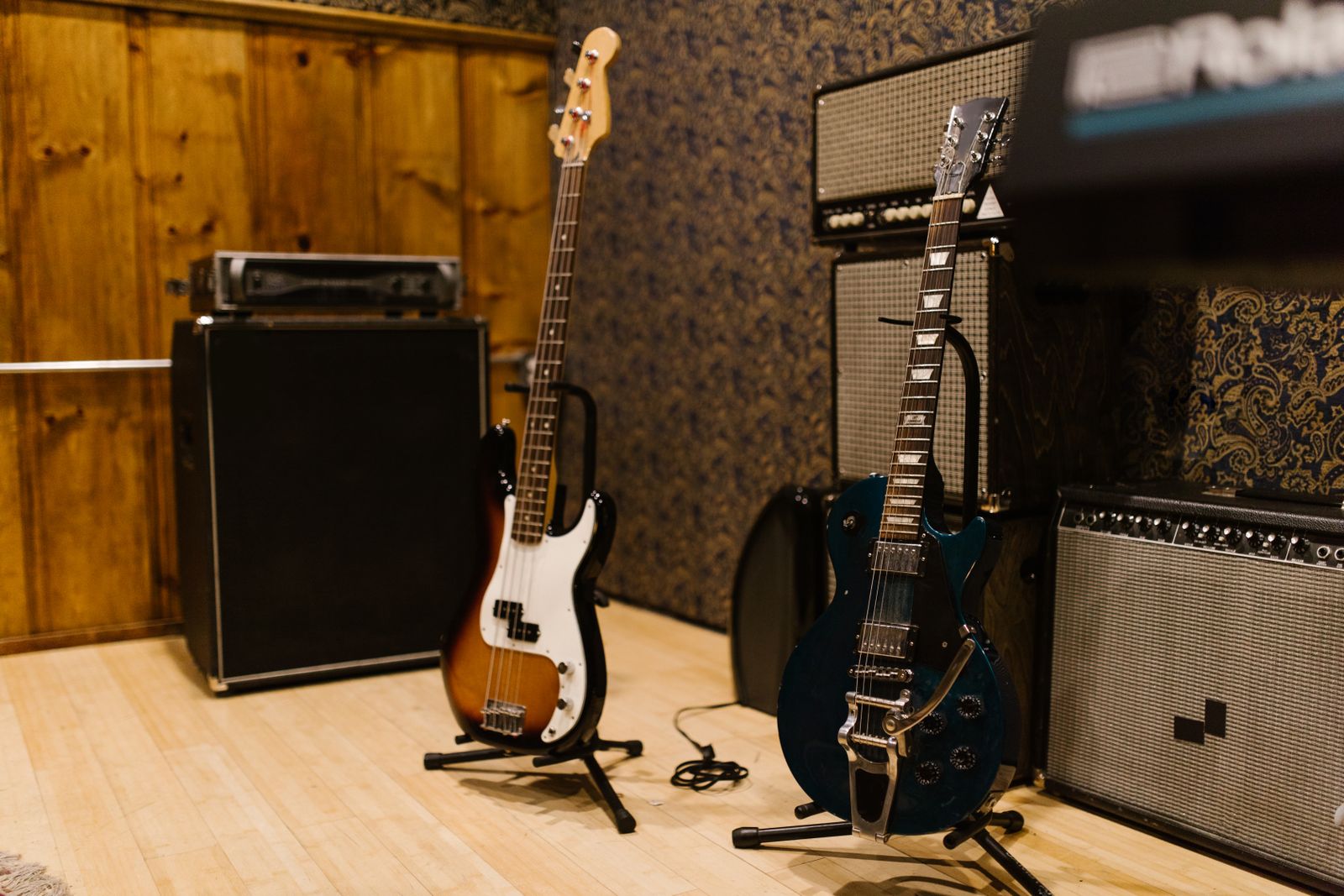 A bass guitar and an electric guitar on stands in a studio next to amplifiers