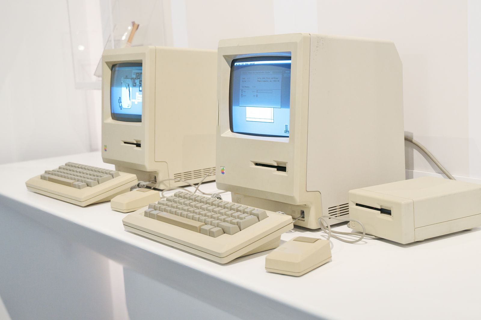Two vintage Macintosh computers showing a graphical interface on their screens