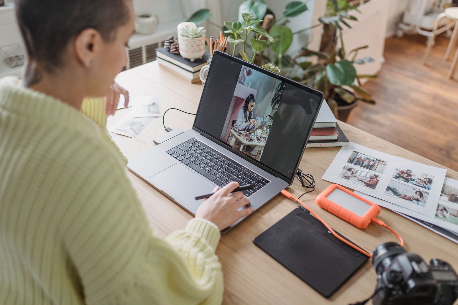 A photographer processing shots on a laptop beside an external drive and prints