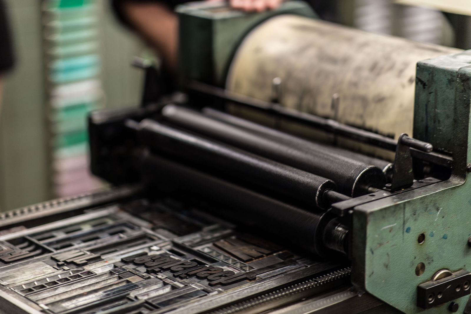 A vintage letterpress machine with rollers in black ink and a type form of metal letters