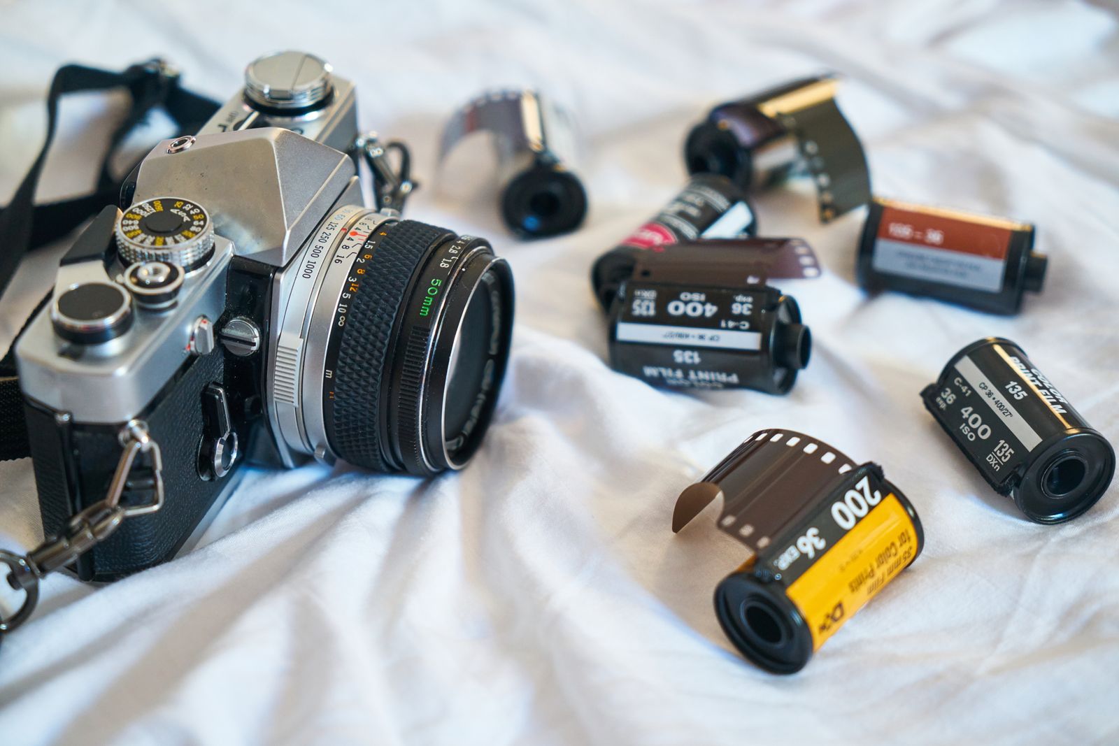 A film SLR camera with a 50mm lens and a scatter of Kodak film rolls — the evolution of media from film to digital codecs